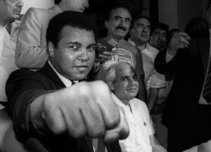 A smiling Muhammad Ali shows his fist to reporters during an impromptu press conference in Mexico City, July 1987. REUTERS/Jorge Nunez