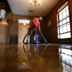 Dalton Hamilton vacuums a flood damaged floor inside a friend’s house in St. Amant