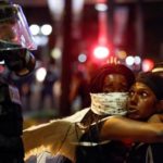 Two women embrace while looking at a police officer in uptown Charlotte, NC during a protest of the police shooting of Keith Scott, in Charlotte