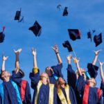 storyblocks/high school students graduates tossing up hats over blue sky.