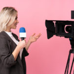 freepik/reporter-woman-holding-microphone-reporting-news-pink-wall_1368-81693