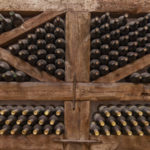 winy-bottles-lie-shelving-from-thick-logs-old-wine-cellars-with-bottles-barrels