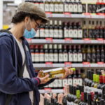 young-man-medical-mask-chooses-wine-supermarket