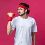 tense-young-sporty-man-wearing-headband-with-wristband-execising-with-dumbbell