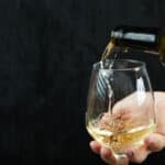 Pouring white wine into the wine glass on dark background. High quality photo