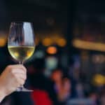 Hand holding a glass of white wine with colorful bokeh light in restaurant.