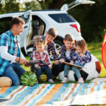 family-spending-time-together-father-reading-book-outdoor-with-kids-against-their-suv-car