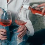 A young couple in blue jeans and white shirts drinks rose wine from glasses