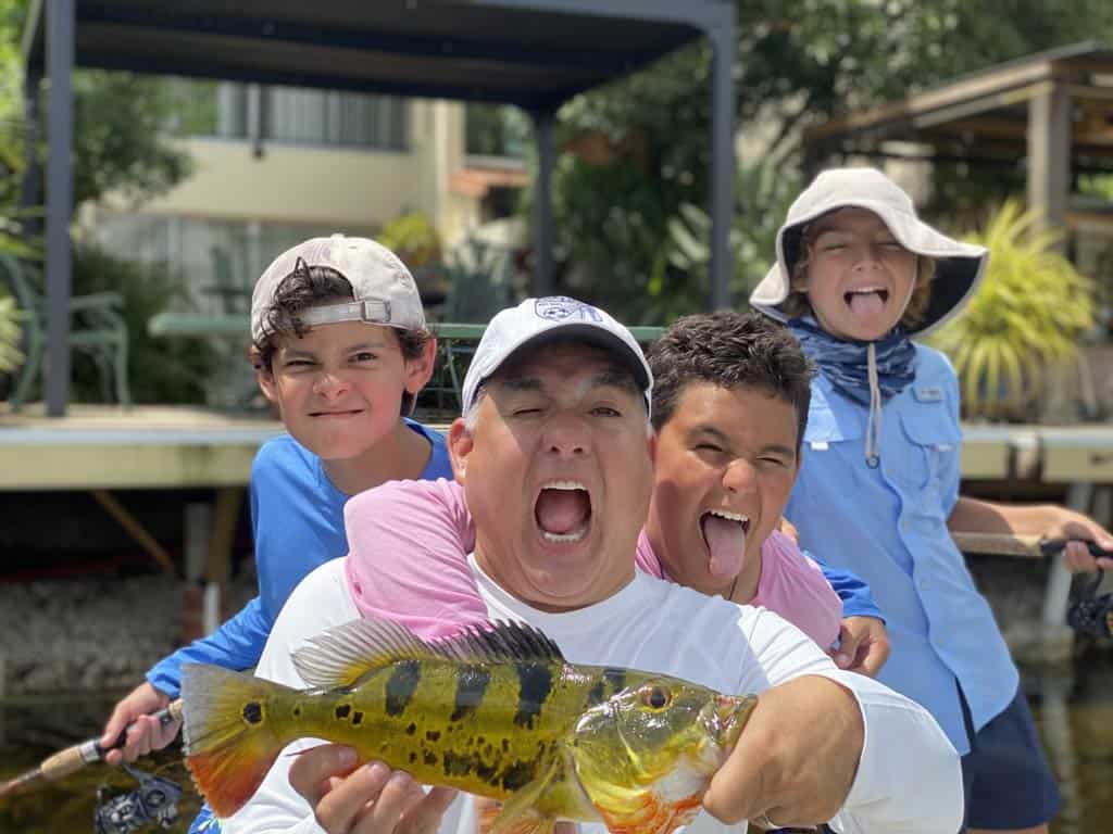 A photo of three kids posing with their dad and making silly faces after catching a Peacock Bass in Florida
